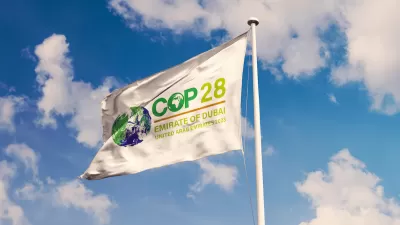 White flag with COP28 cliamte conference logo against lightly cloudy blue sky.