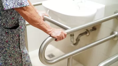 Close-up of woman in flowered dress holding bar next to white porcelain sink in bathroom.