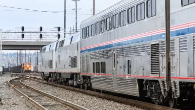 Silver and blue Amtrak train approaching an oncoming orange freight train at station in Seattle, Washington.