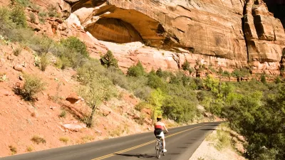 Person on bike wearing helmet biking on asphalt road with red cliffs in background in Zion National Park