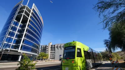 Green Tempe streetcar with downtown Tempe glass building in background.