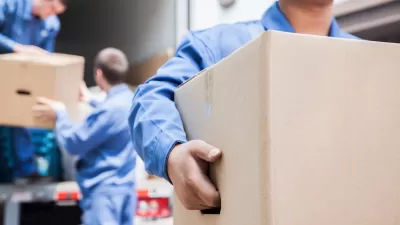 Blurred close-up of movers in blue coveralls unloading cardboard boxes from moving van.