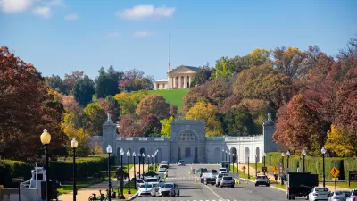 View of street in front of Arlington National Cemetery with ornate neoclassical building on hilltop in background.