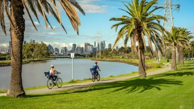 Two people on bikes on a riverbank trail in Melbourne, Australia with city skyline in background