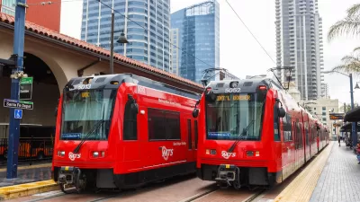 Two red San Diego trolley cars at Santa Fe Depot station with high-rise buildings in background.