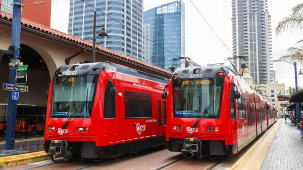 Two red San Diego trolley cars at Santa Fe Depot station with high-rise buildings in background.