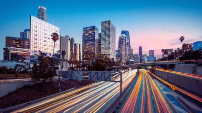 Blurred traffic speeding by on freeway with Los Angeles skyline in background.