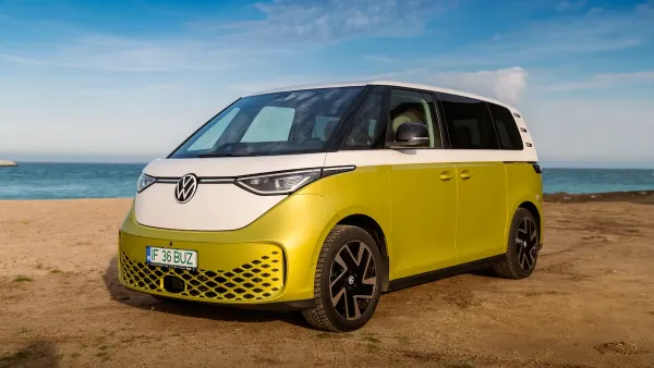 Green electric Volkswagen van against a beach backdrop.