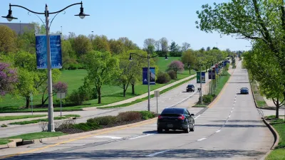 Wide suburban road with landscaped median and light pole banners advertising local amphitheater.