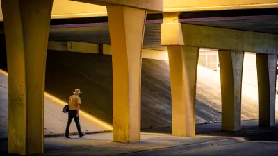 Man in wide-brimmed hat walks through nondescript concrete freeway underpass.