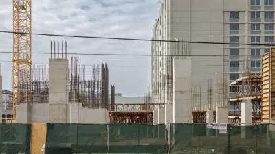 Multistory concrete apartment building under construction behind green construction fence.