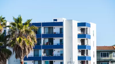 Top floors of blue and white apartment building with palm trees against sunny blue sky in Malibu, California.