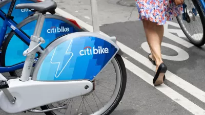 Close-up of Citi Bike electric bikes at on-street station in New York City next to bike lane with woman walking a bike.