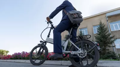 Person on folding electric bike wearing messenger bag resting foot on ground on urban street.