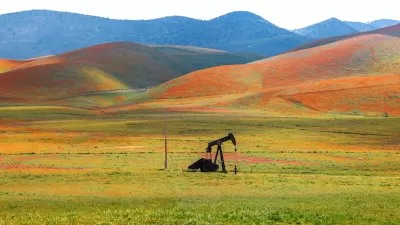 Abandoned oil well against hill covered in blooming orange flowers in Carrizo Plain National Monument, California.