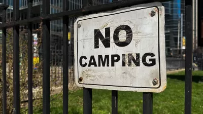 Close-up of white and black NO CAMPING sign on black iron fence.