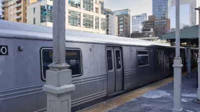 Silver train at station on elevated track with city high-rises in the background.