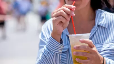 Close-up of woman in blue and white striped button-up shirt drinking from clear plastic cup with red straw.