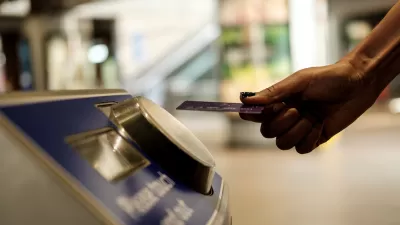 Close-up of hand holding transit card up to fare collection machine in transit station.