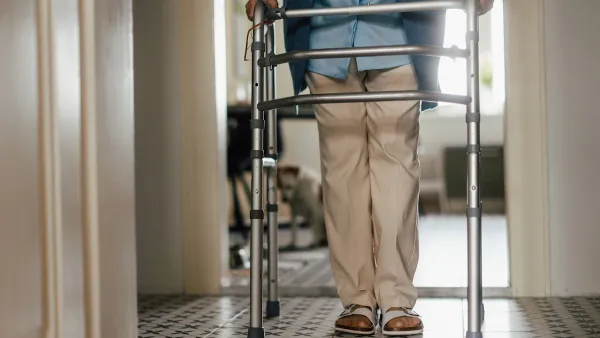 Close-up of elderly person walking inside home leaning on walker.