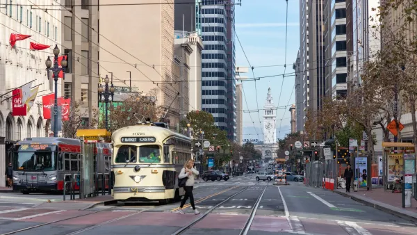 Streetcar and bus stopped at station on Market Street in San Francisco with Ferry Building visible in background.