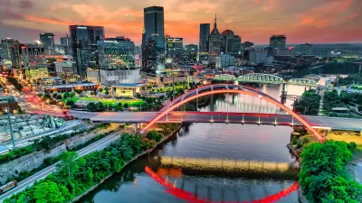Aerial view of Nashville, Tennessee skyline with river and bridge in foreground against sunrise or sunset sky.