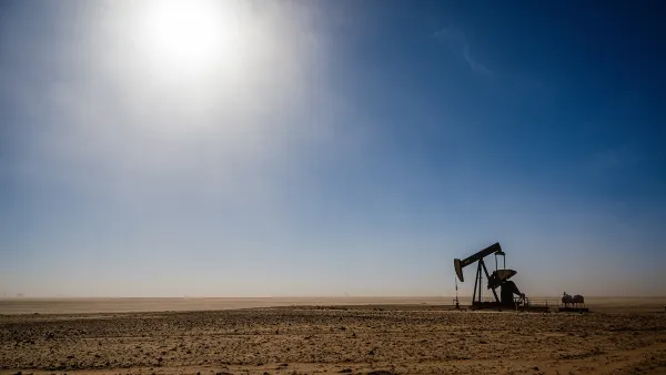 Distant view of oil derrick on barren plain with harsh sun in background.