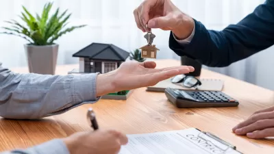 Close-up of person signing home or apartment contract and receiving house key with house-shaped keychain.