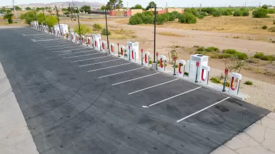Vacant Tesla charging station in asphalt parking lot next to Interstate 10 in Arizona.