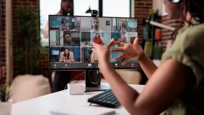 Person wearing headphones sitting at desk with monitor showing other people on Zoom meeting.