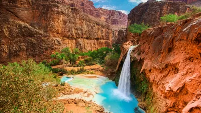 View of Havasu Falls with bright turquoise water and a canyon winding through red vertical cliffs in the Grand Canyon