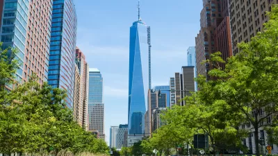 View of One World Trade Center down straight street with bright green trees on either side.
