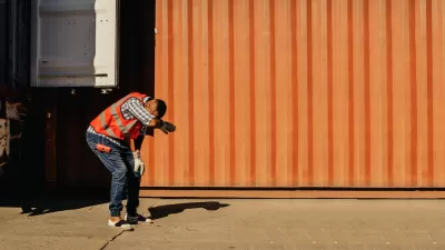 Worker in safety vest leaning over expressing heat exhaustion standing next to orange shipping container.