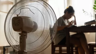 Close-up of floor fan operating with blurred woman sitting at table in background.