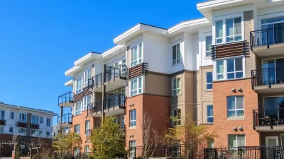 Four-story modern apartment complex with white stucco and red brick.
