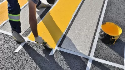 Close-up of man painting white and yellow crosswalk on asphalt.