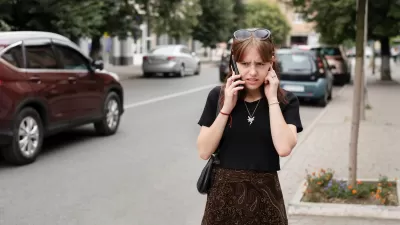 Girl on phone struggling to hear standing on loud city street.