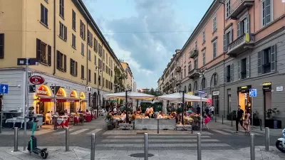 Pedestrianized street in Milan, Italy with outdoor dining tables and umbrellas.