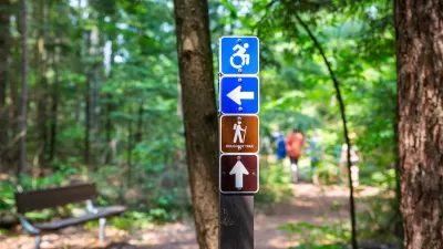 Sign showing accessible hiking trail sign with blurred forest in background.