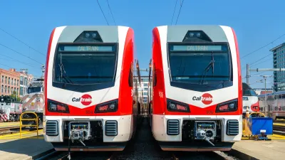 Two white and red Stadler electric Caltrain trains next to each other on a sunny day.