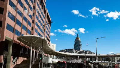 Red bus parked at transit station in Denver, Colorado with CO state capitol dome in background.