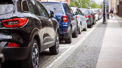Curbside packed with park cars and cyclist riding on the sidewalk.