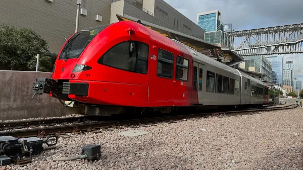 Red modern train on tracks with large warehouse-type building behind it in Austin, Texas.
