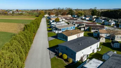 Aerial view of mobile home community in rural area with homes lined up diagonally next to small road.