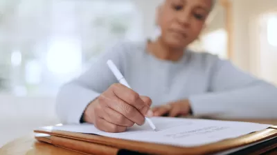 Older black woman writes on document with a pen.