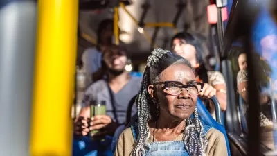 Older Black woman with glasses and braids sitting on city bus, looking out window.