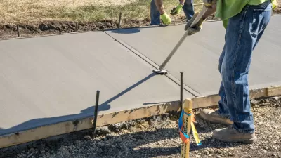 Workers pouring concrete in wooden mold for new sidewalk