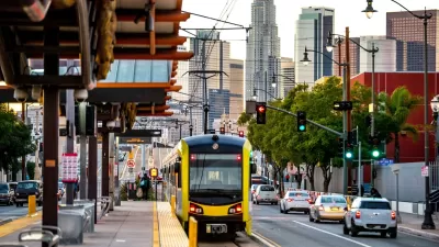 Yellow and black Metro light rail train pulling up to outdoor platform with Los Angeles skyline in background.