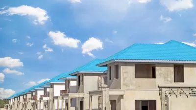 Row of concrete two-story homes with blue tile roofs under construction.