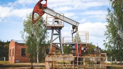 Old oil well with red brick building in the background.